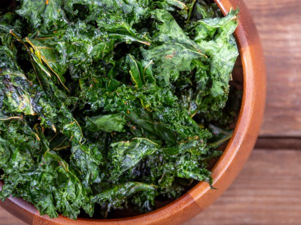 healthy homemade seasoned green kale chips snack on a wooden bowl over a plank table
