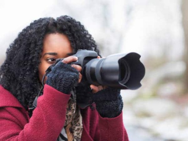 A woman outdoors with a digital SLR camera taking pictures on a winter day.